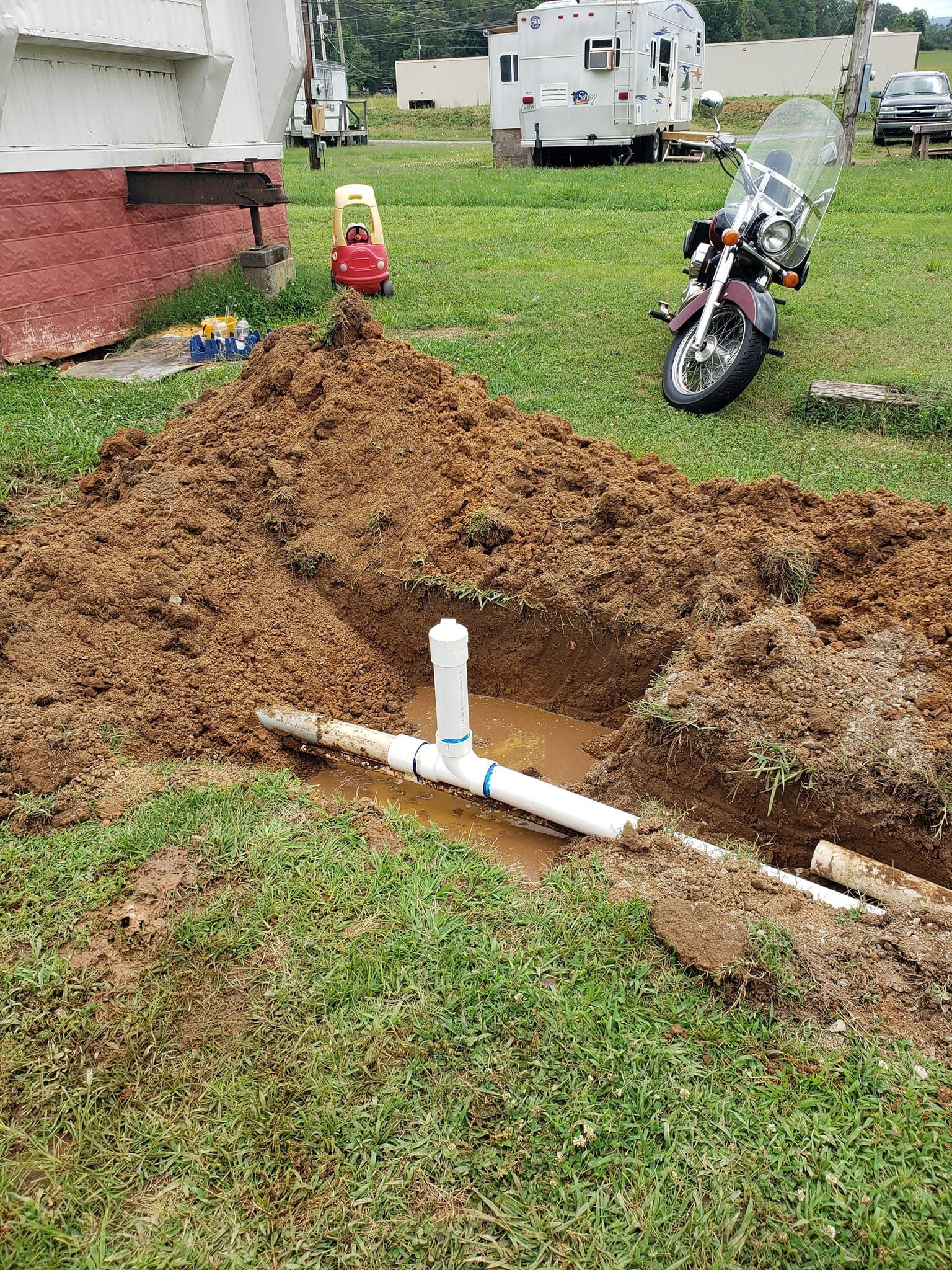 A motorcycle is parked in the dirt next to a hole in the ground.