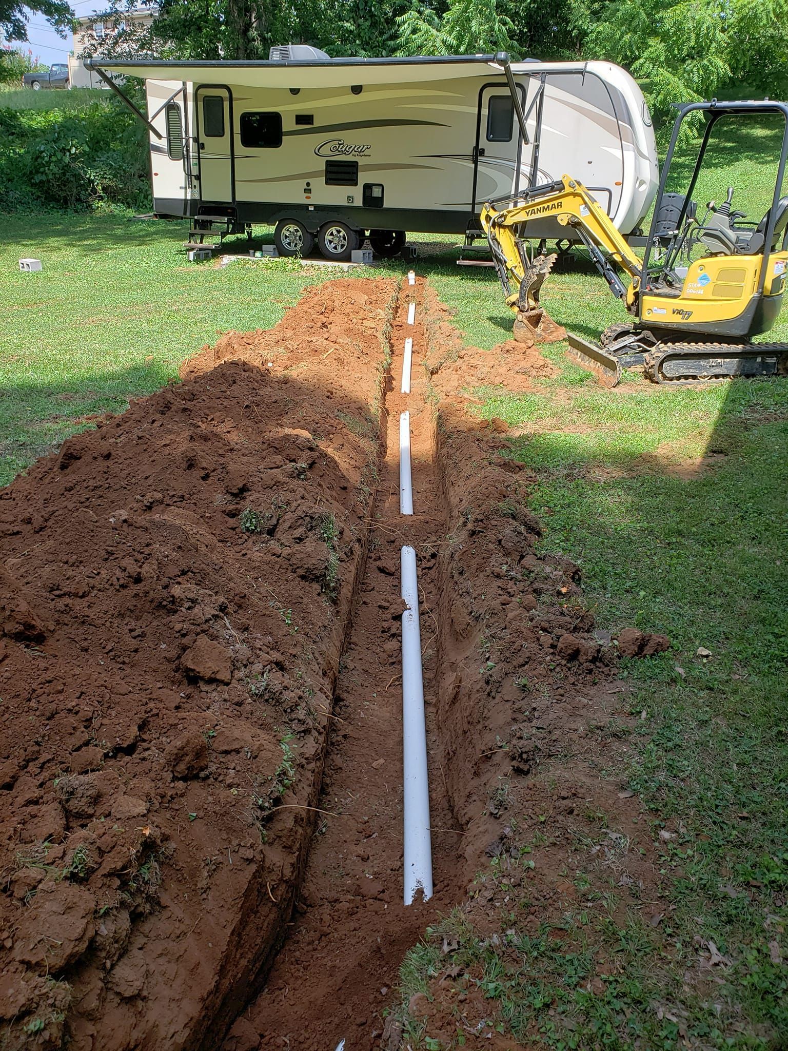 A hose is being installed in the dirt next to a trailer.