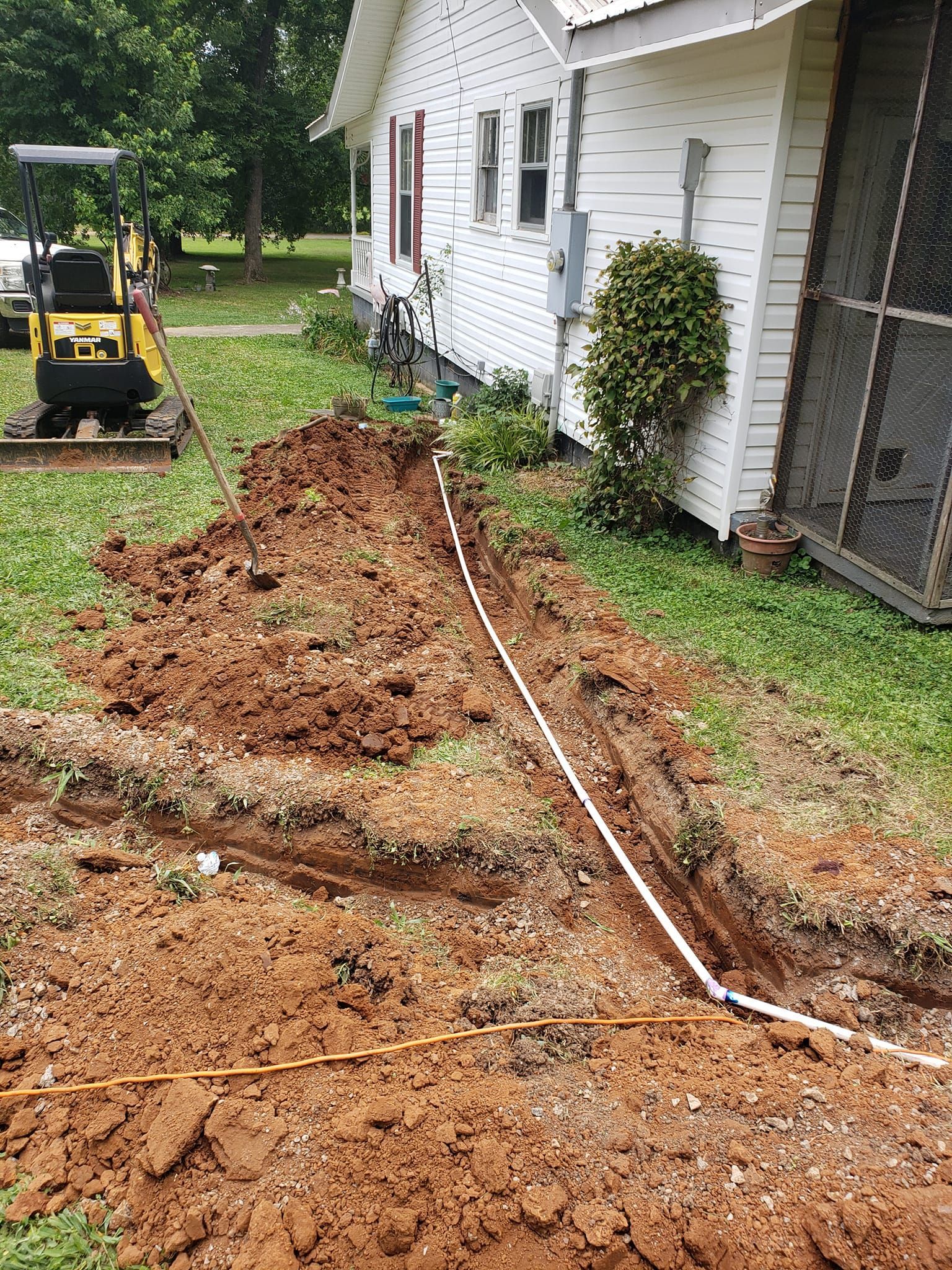 A bulldozer is digging a hole in the dirt in front of a house.