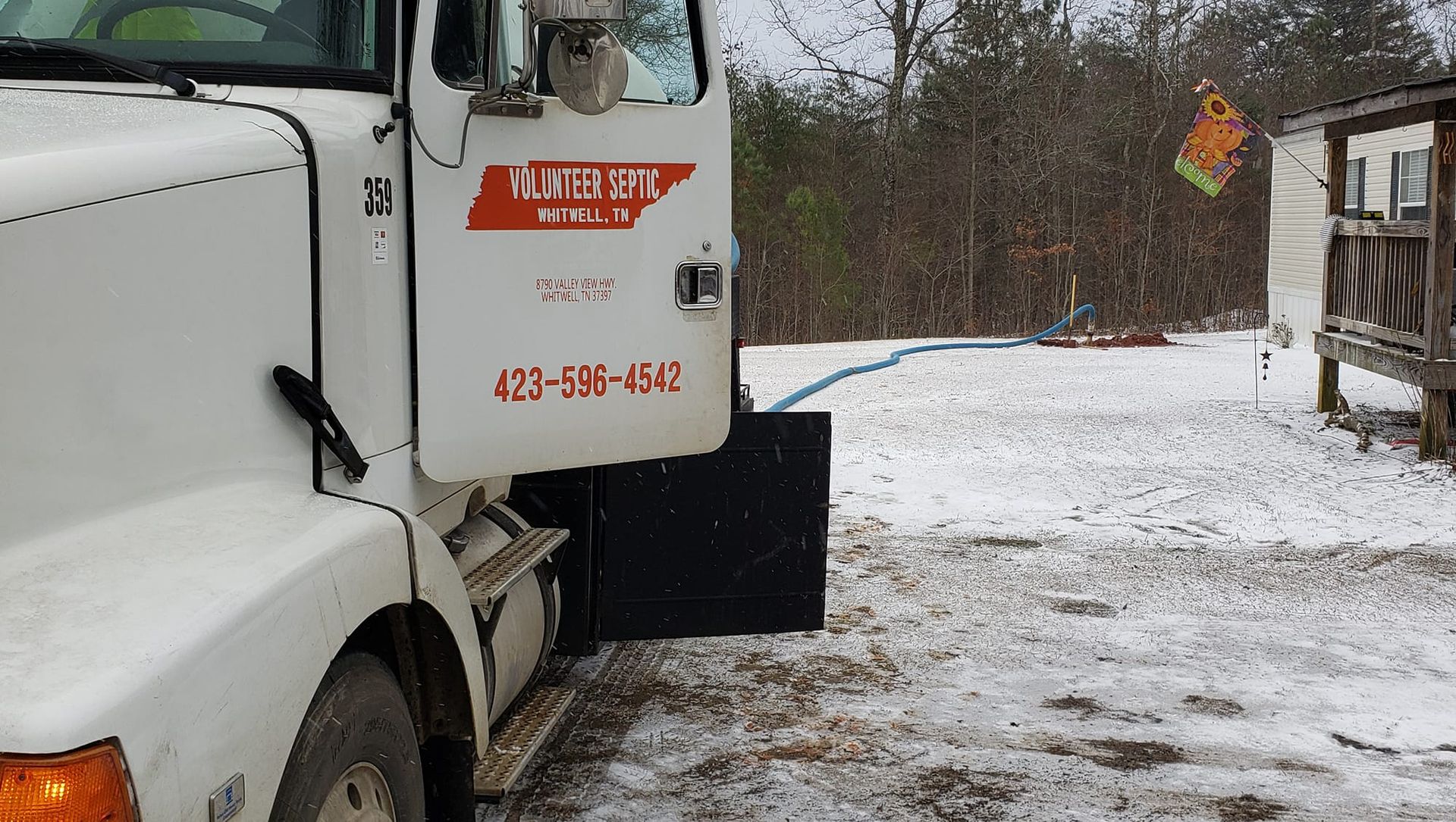 A white truck is parked in the snow with a phone number on the door