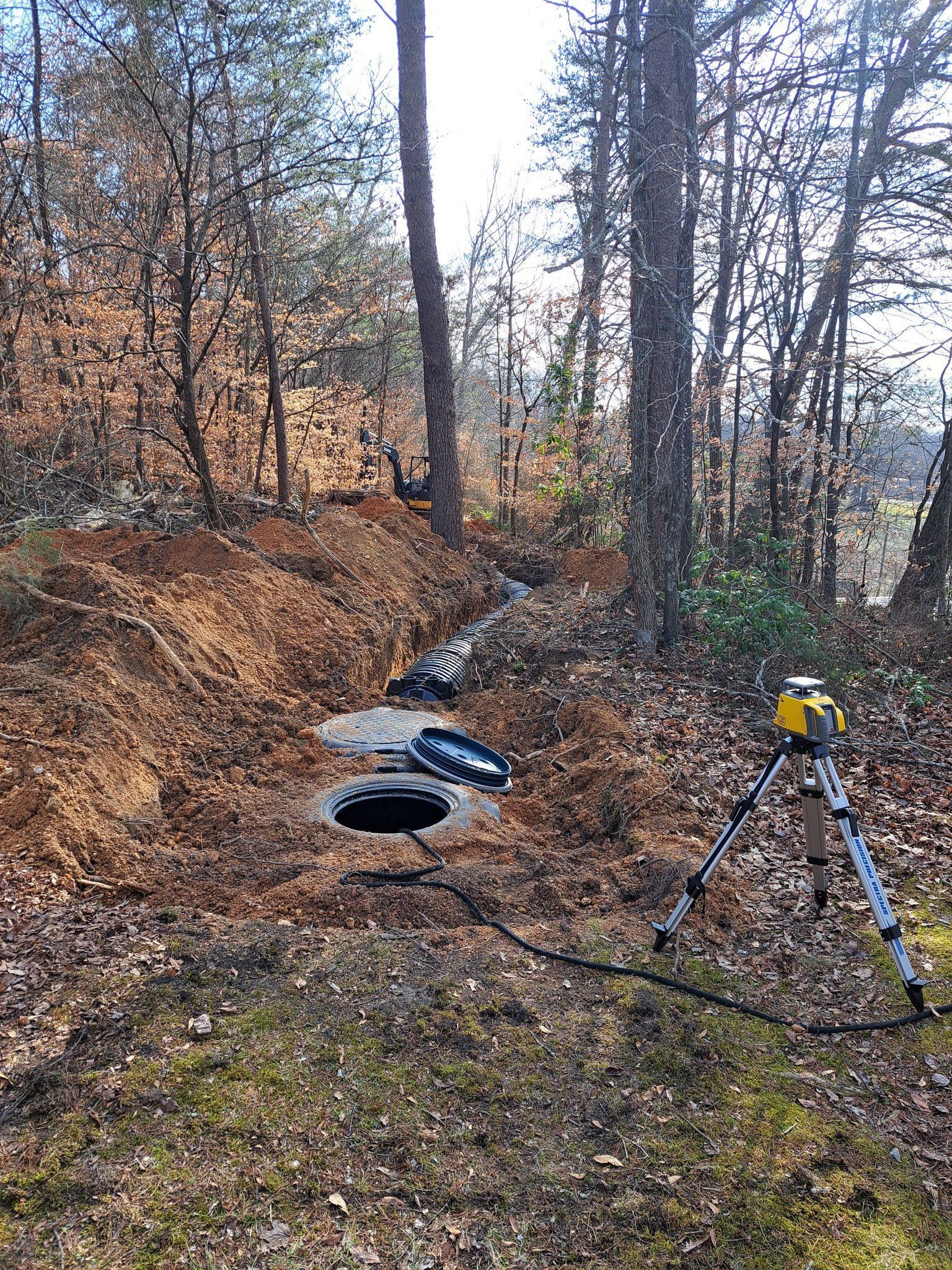 A manhole cover is sitting in the middle of a forest next to a tripod.