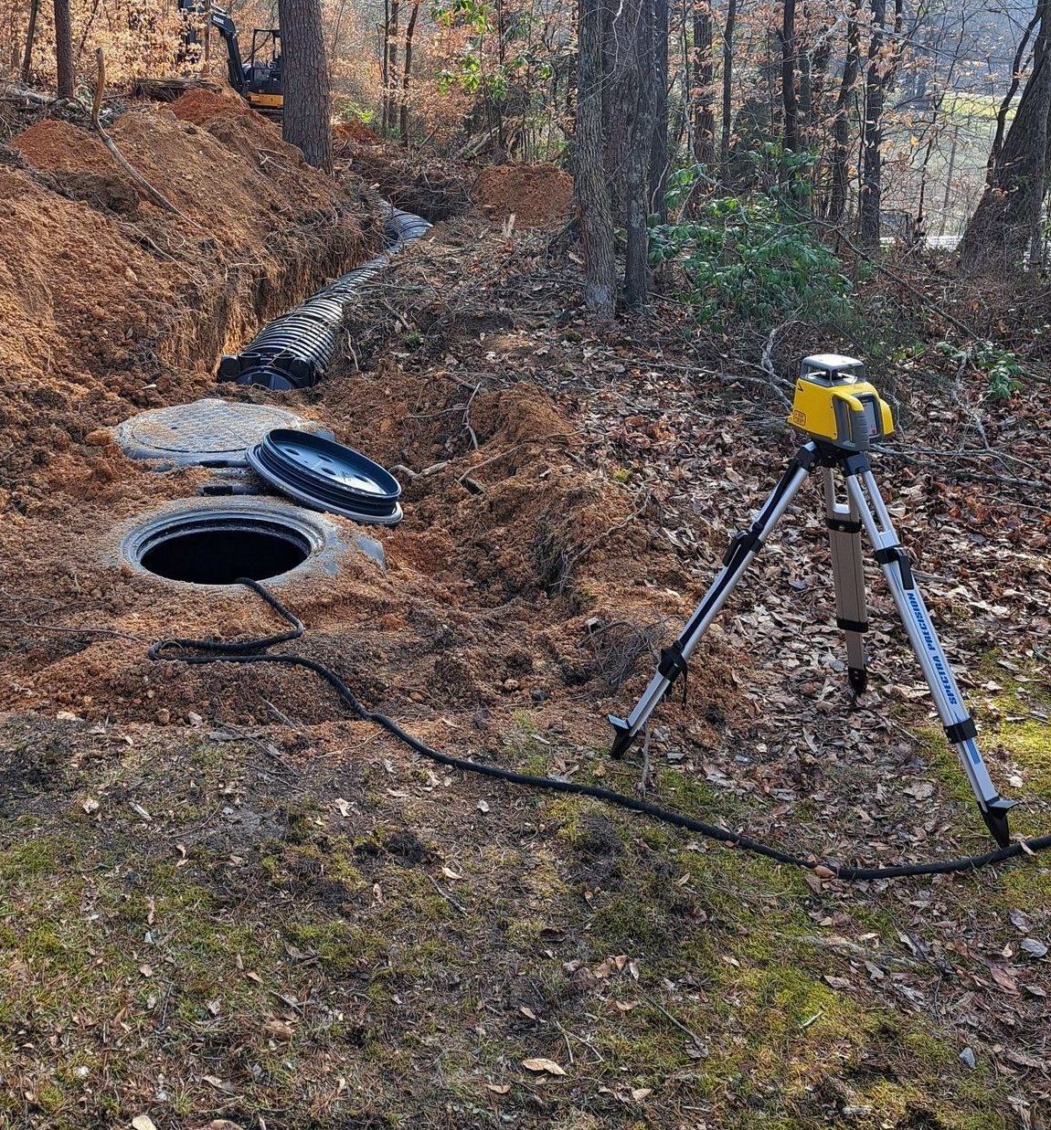 A tripod is sitting next to a manhole in the woods.