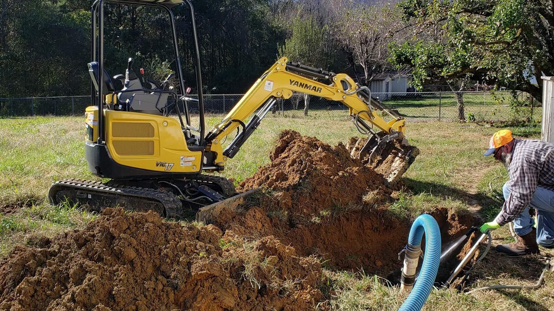 A yellow excavator is digging a hole in the dirt in a field.