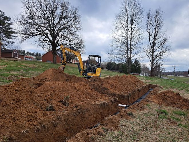 A yellow excavator is digging a hole in the dirt in a field.