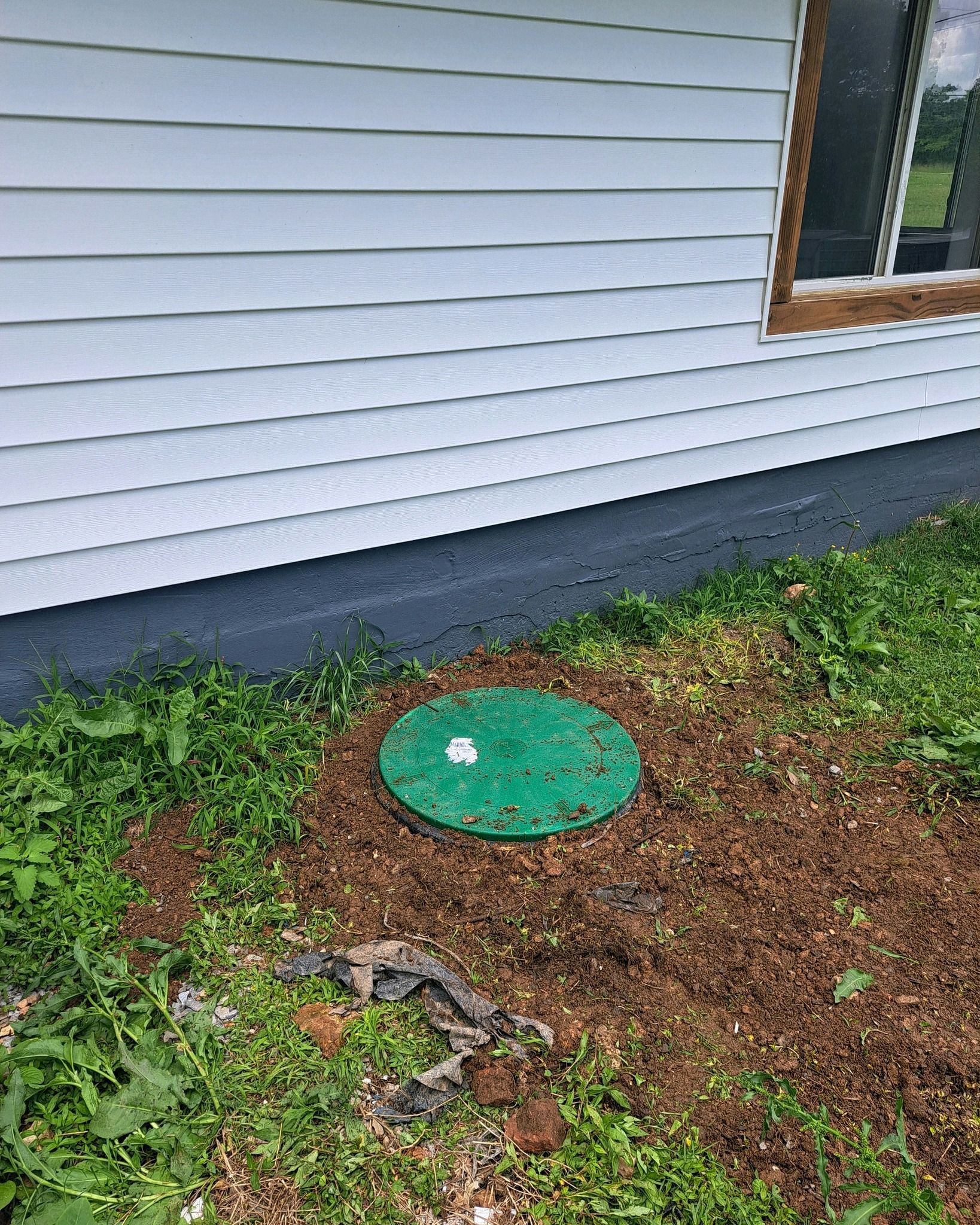 A green septic tank is sitting in the grass in front of a house.