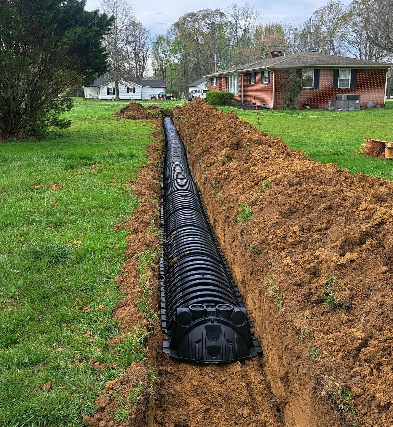 A drainage system is being installed in a yard next to a house.