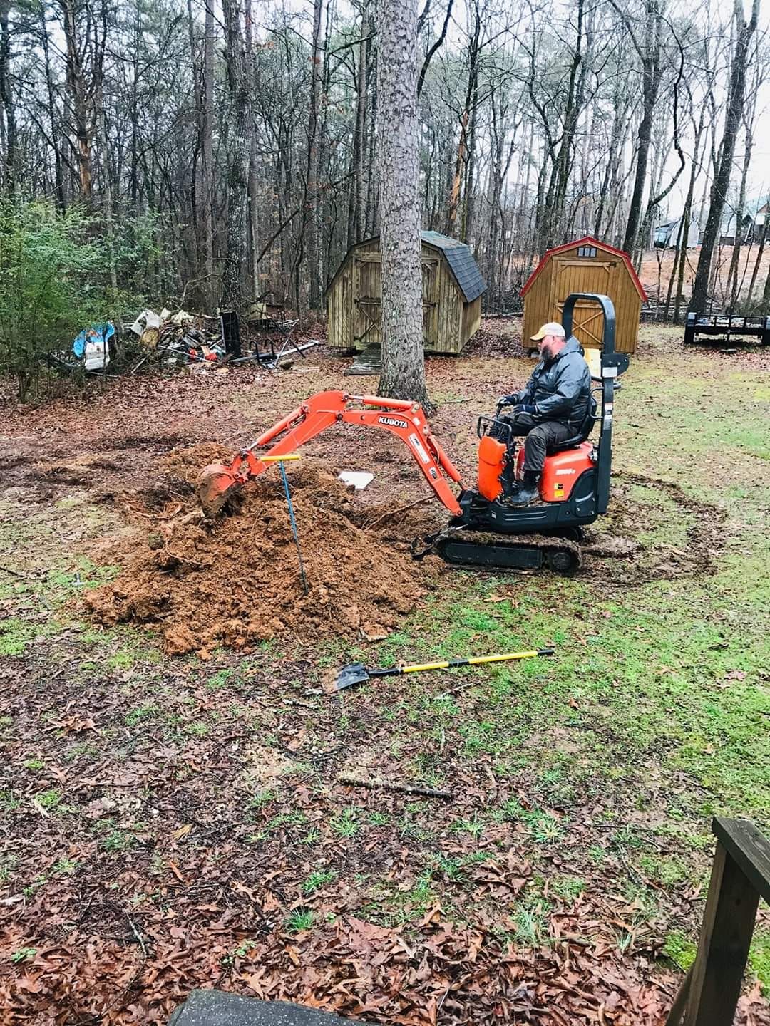 A man is driving a small excavator in a yard.