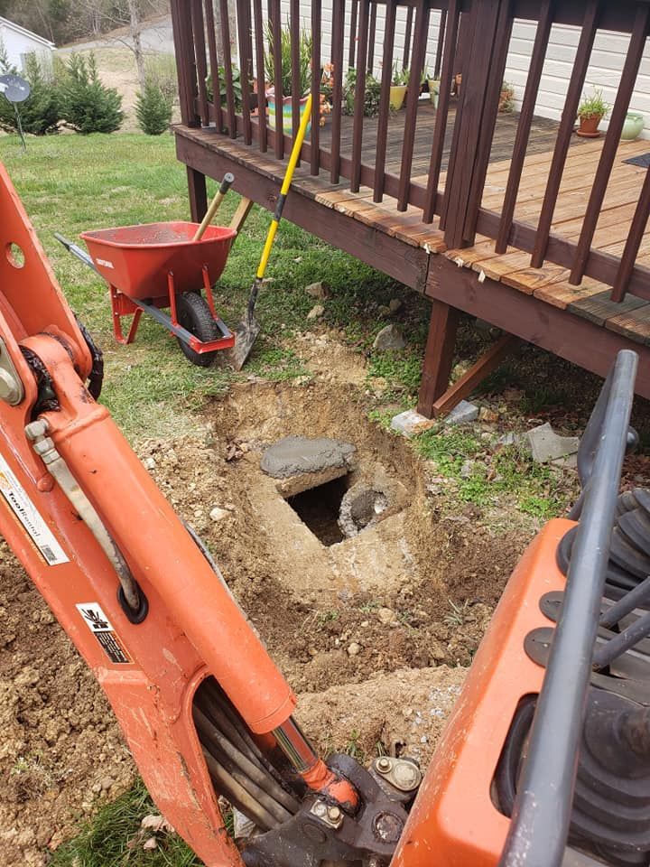 An excavator is digging a hole under a deck next to a wheelbarrow.