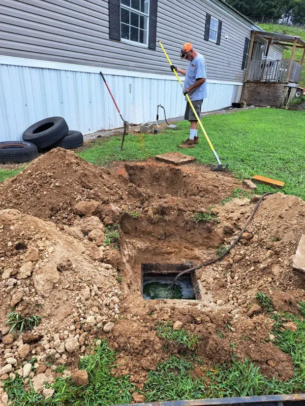 A man is digging a hole in the ground in front of a mobile home.