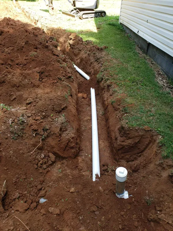 A white pipe is laying in the dirt next to a house.