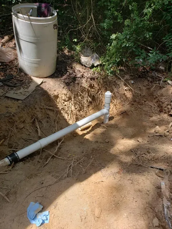 A white bucket is sitting next to a pipe in the dirt.