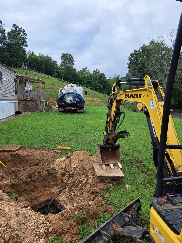 A yellow excavator is digging a hole in the ground in front of a house.