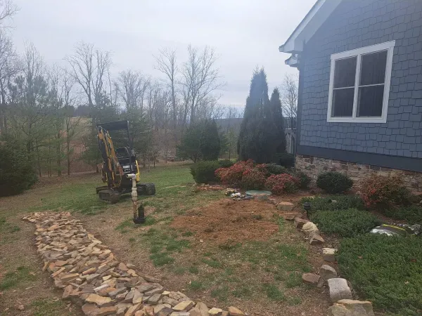 A small excavator is sitting in front of a blue house.