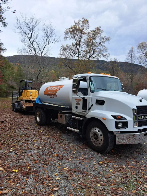 A white tanker truck is parked in a gravel lot next to a yellow forklift.
