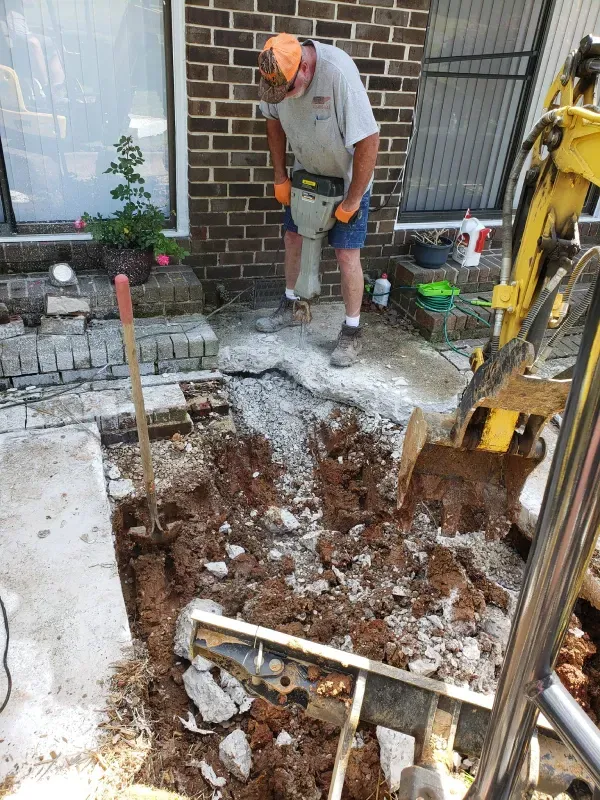 A man is using a hammer to break concrete in front of a brick building.
