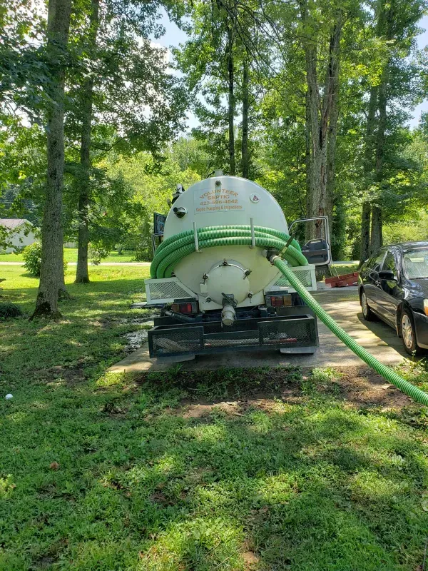 A septic tank truck is parked in a grassy yard next to a car.