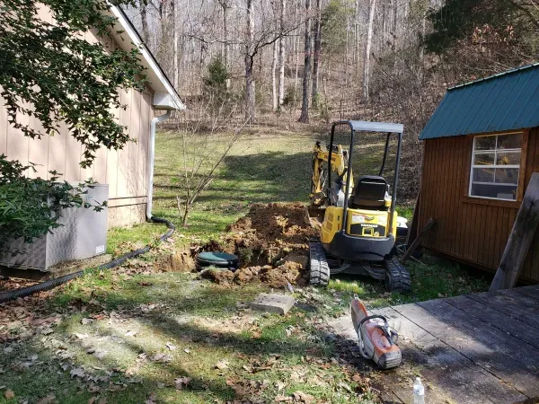 A yellow excavator is digging a hole in a yard next to a house.