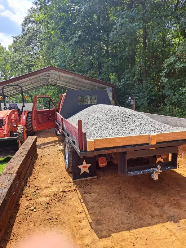 A dump truck filled with gravel is parked next to a tractor.