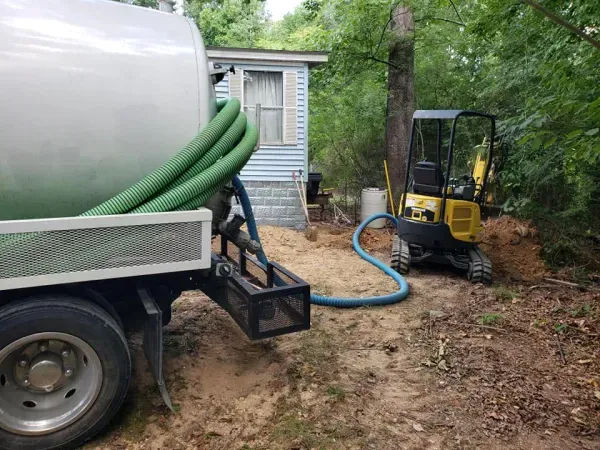 A septic tank truck is pumping water into a small excavator.