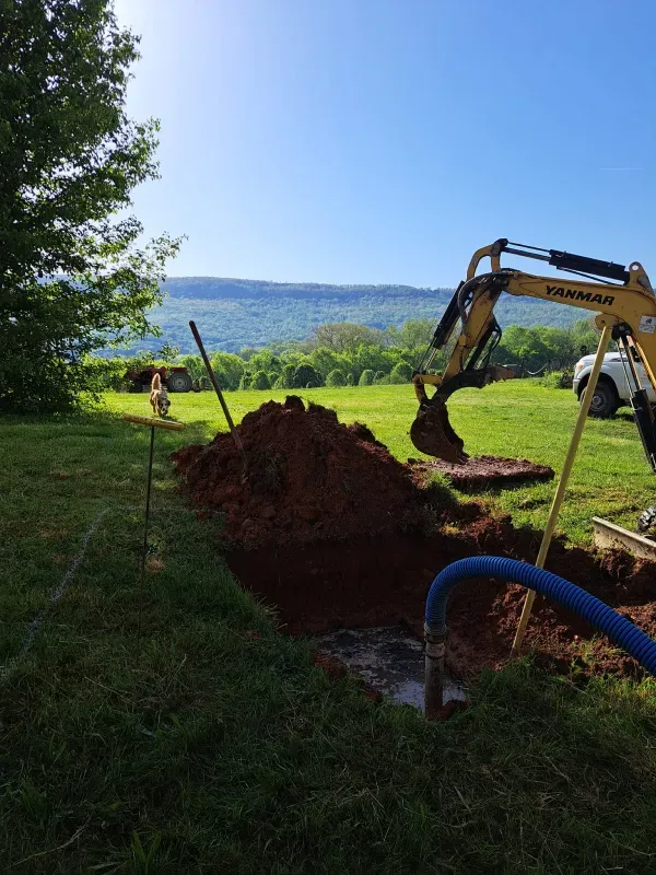 A yellow excavator is digging a hole in a grassy field.