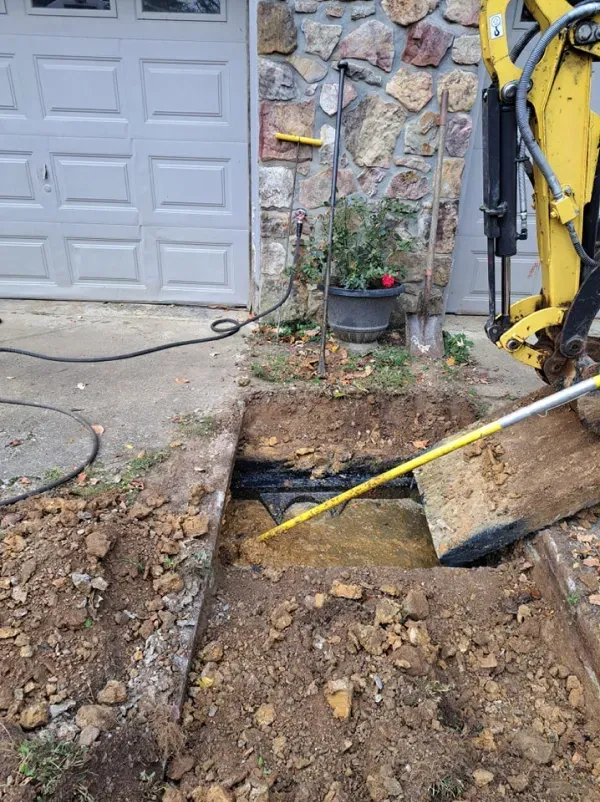 A yellow excavator is digging a hole in the ground in front of a garage door.