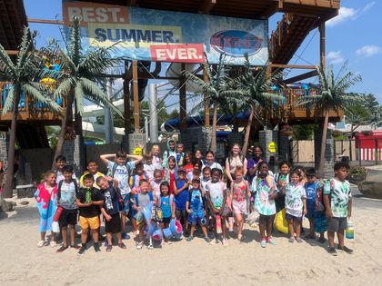 A group of children at a water park stand in front of water slides, under a sign that says 