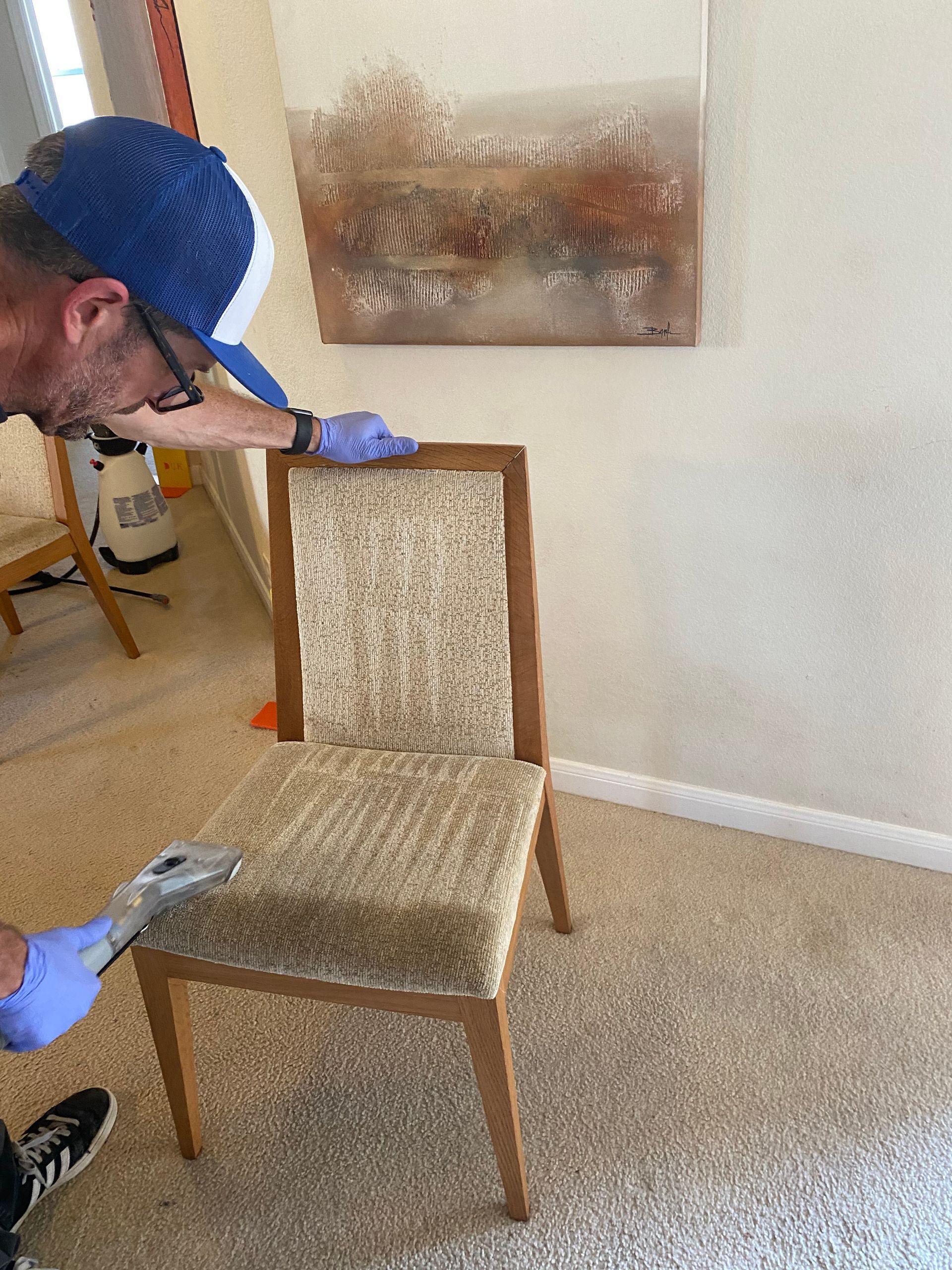 A man is cleaning a couch with a vacuum cleaner.