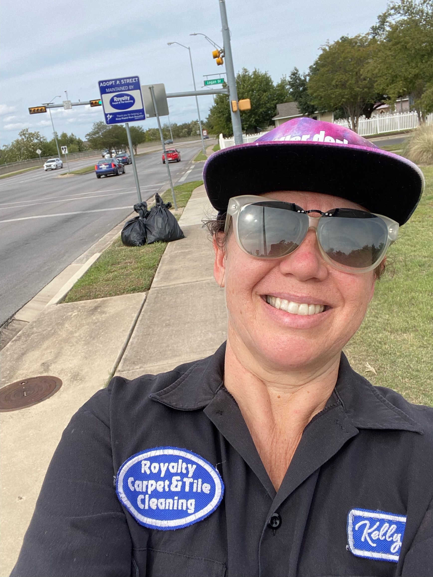 A woman wearing sunglasses and a hat is standing on a sidewalk.