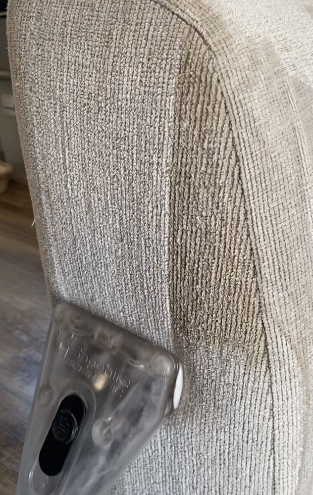 A person is cleaning a couch with a vacuum cleaner.