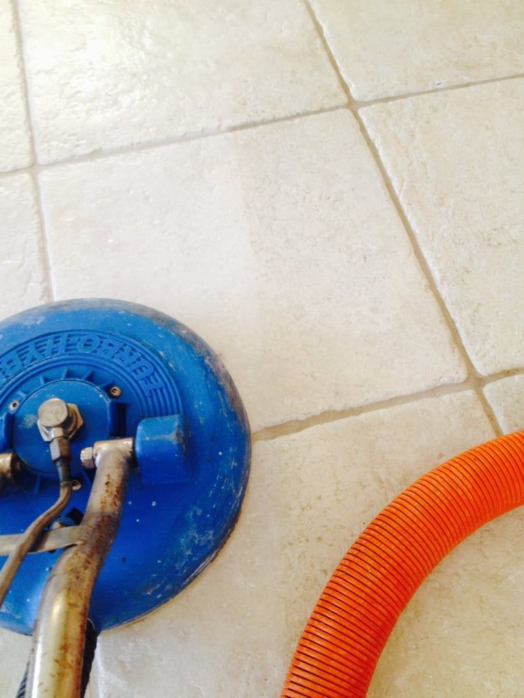 A blue vacuum cleaner is sitting on a tiled floor next to an orange hose.