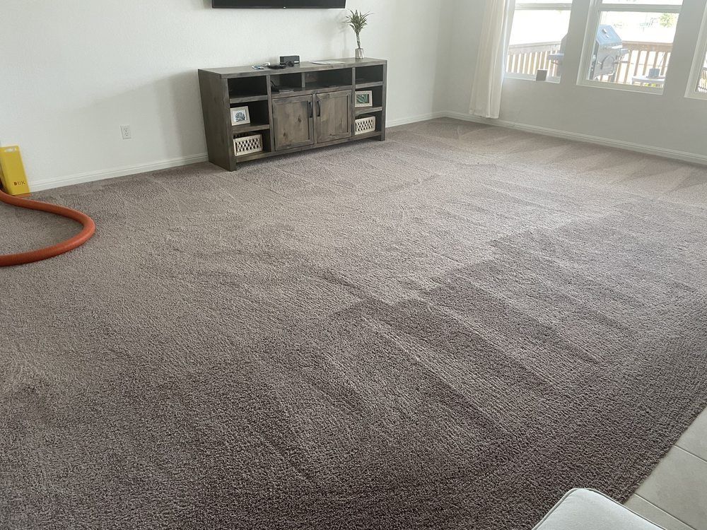 A living room with a large carpeted floor and a television on the wall.