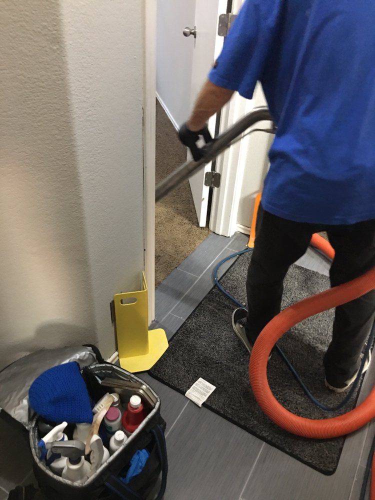 A man in a blue shirt is using a vacuum cleaner to clean a doorway.