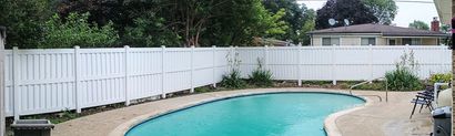 A backyard with a swimming pool, white fence, trees, and a house.