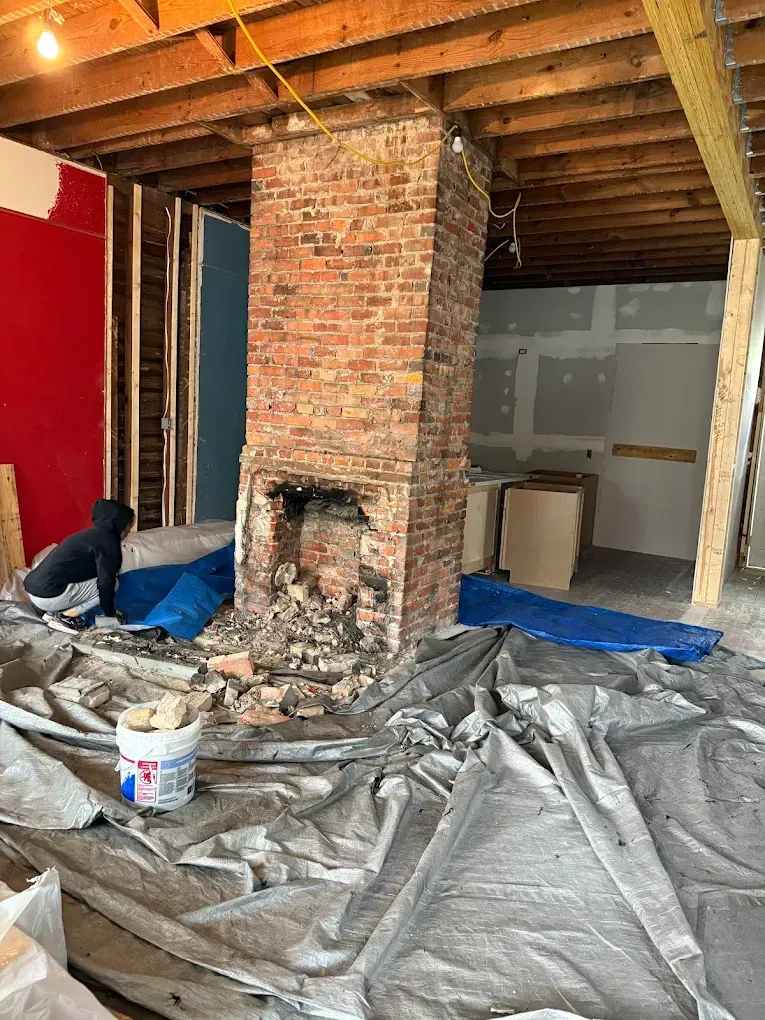 Renovated interior with a brick chimney, debris on tarps, and a person working.
