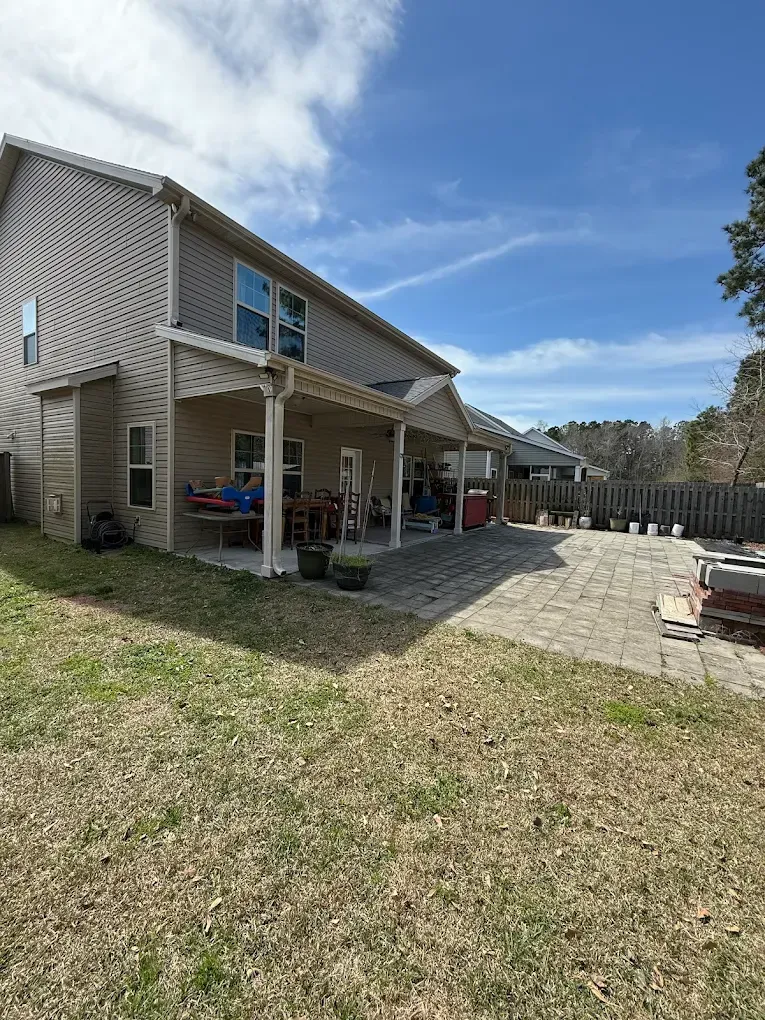 Back of a two-story house with a covered patio and brick patio on a sunny day.