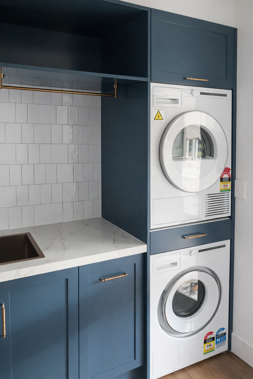 Laundry Room with A Stacked Washer and Dryer, Sink, Cabinets, Window with Blinds, and Laundry Baskets — Paul Tagget Kitchens In Goonellabah, NSW