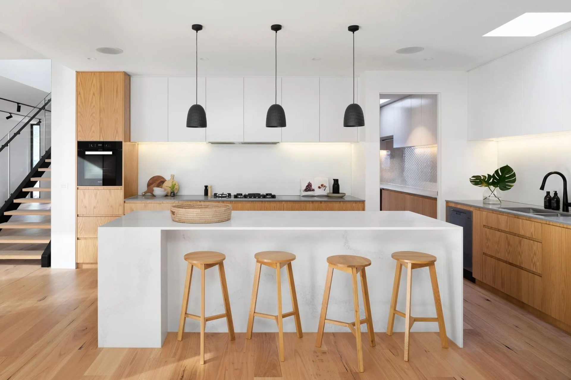 Modern Kitchen With Light Wood Cabinets, White Countertops, Island With Stools, and Black Pendant 