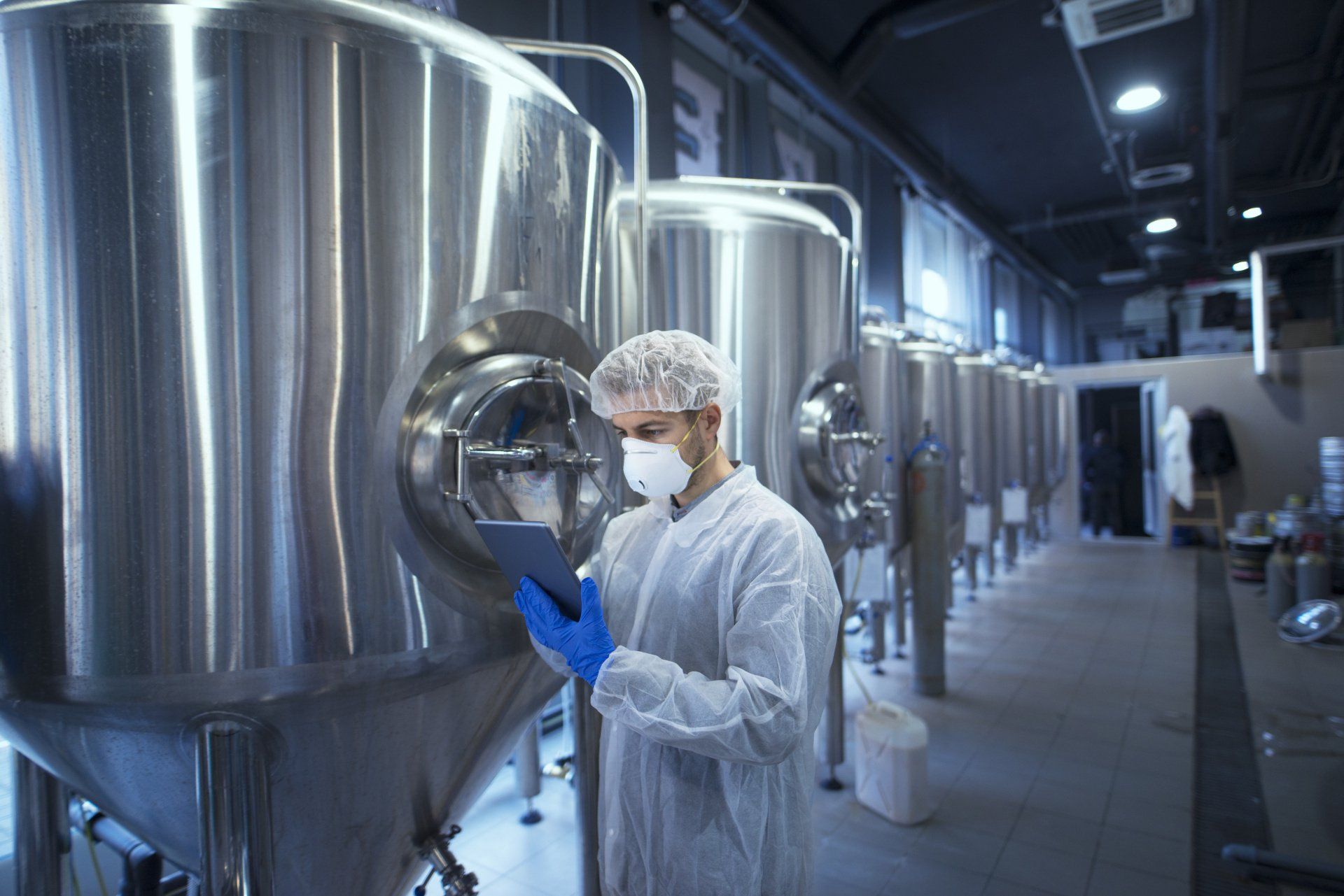 A man in a lab coat is looking at a tablet in a factory.