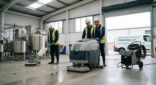 Workers cleaning industrial equipment in a warehouse with polishing machines and stainless steel tanks.