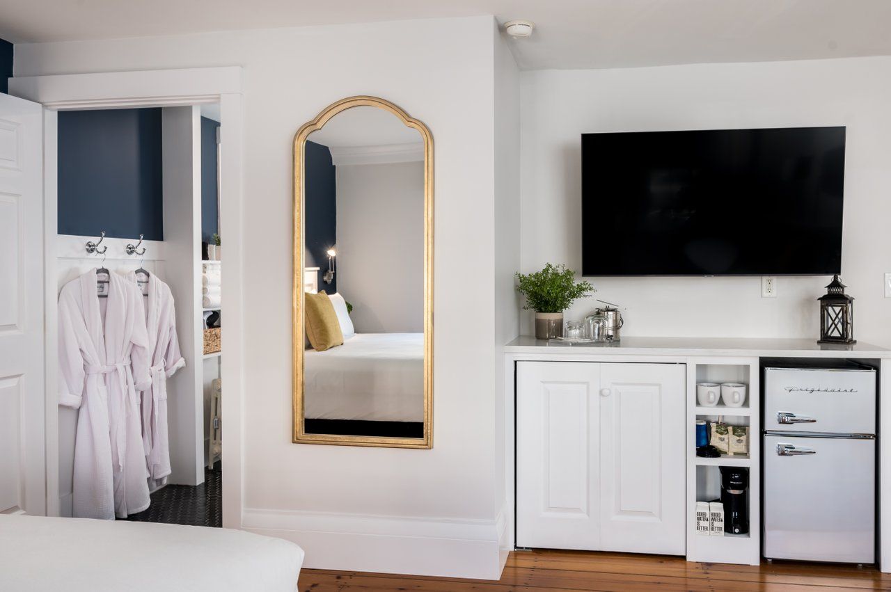 A hotel room with a large mirror , a flat screen tv , and a refrigerator.