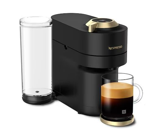 A black Nespresso coffee machine with a clear water tank, next to a glass mug of freshly brewed coffee on a gold base.