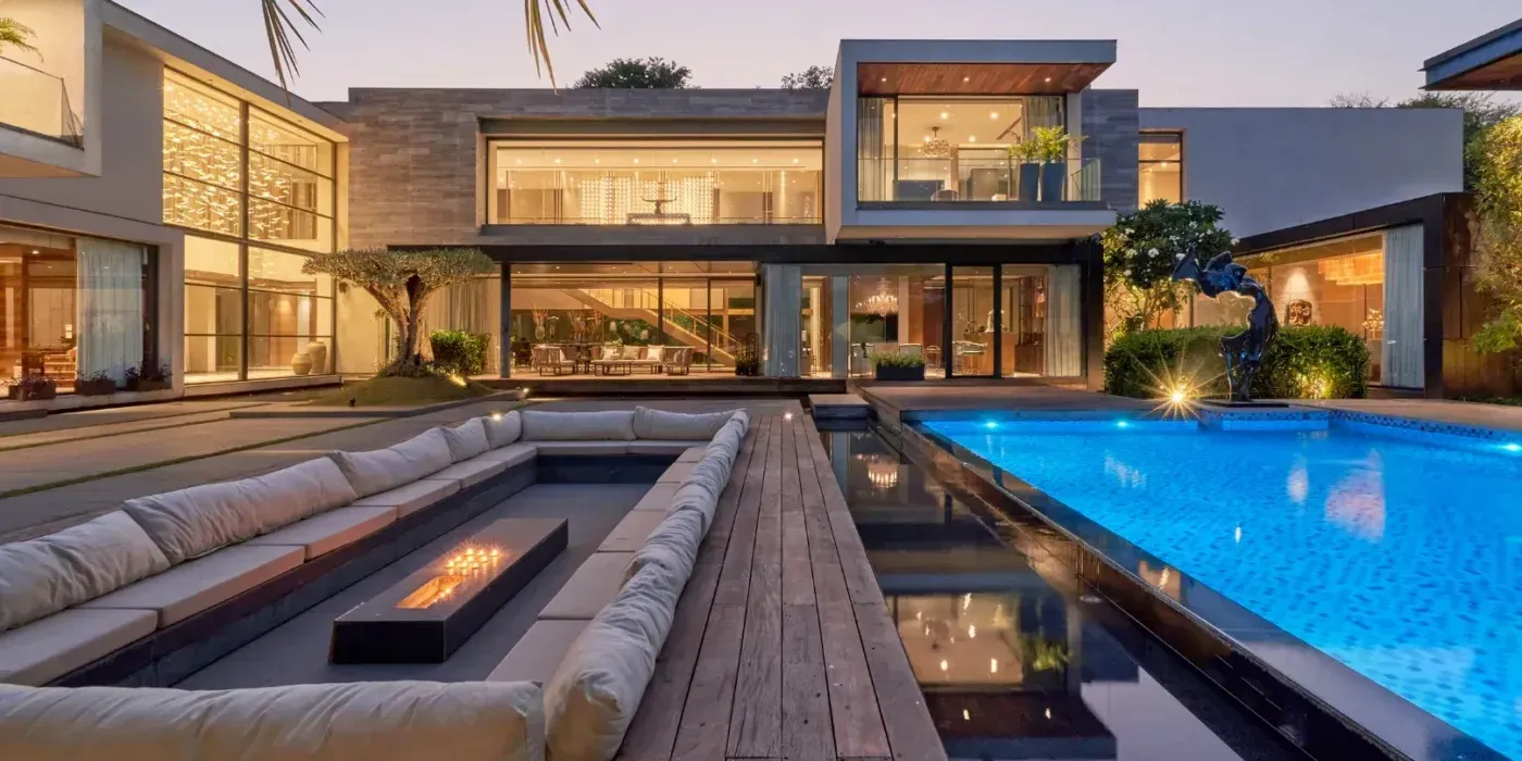Modern luxury home patio with glowing fire pit and lit swimming pool at dusk