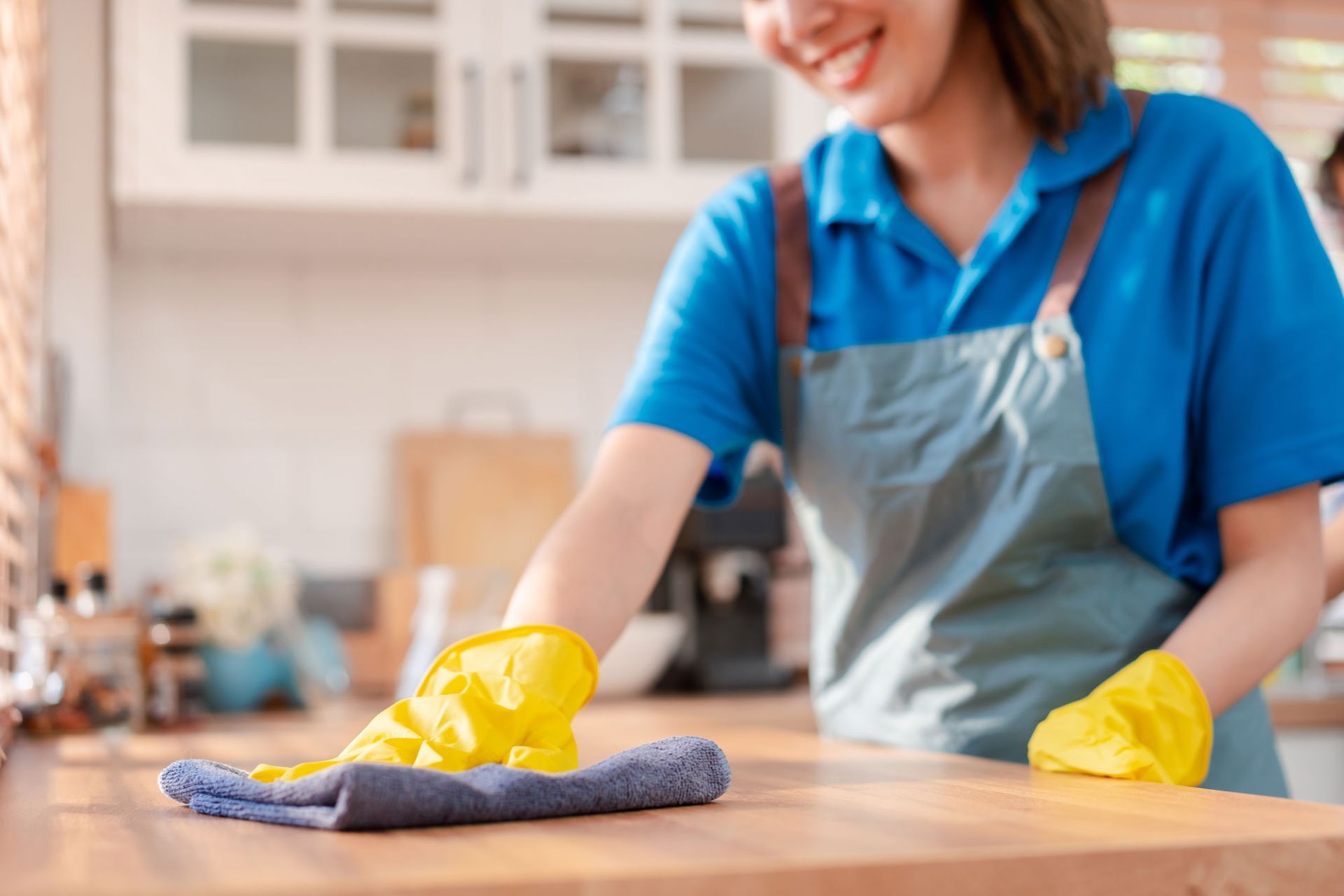 A woman is cleaning a kitchen counter with a cloth and gloves.