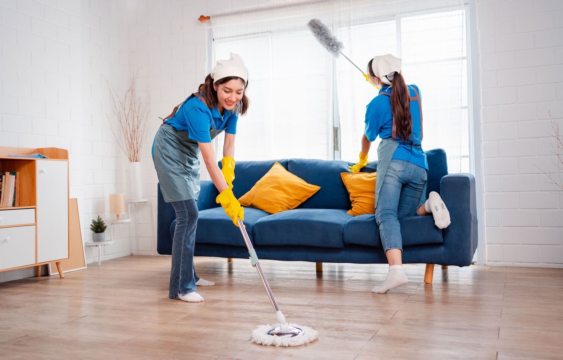 Two women are cleaning a living room with a mop and duster.