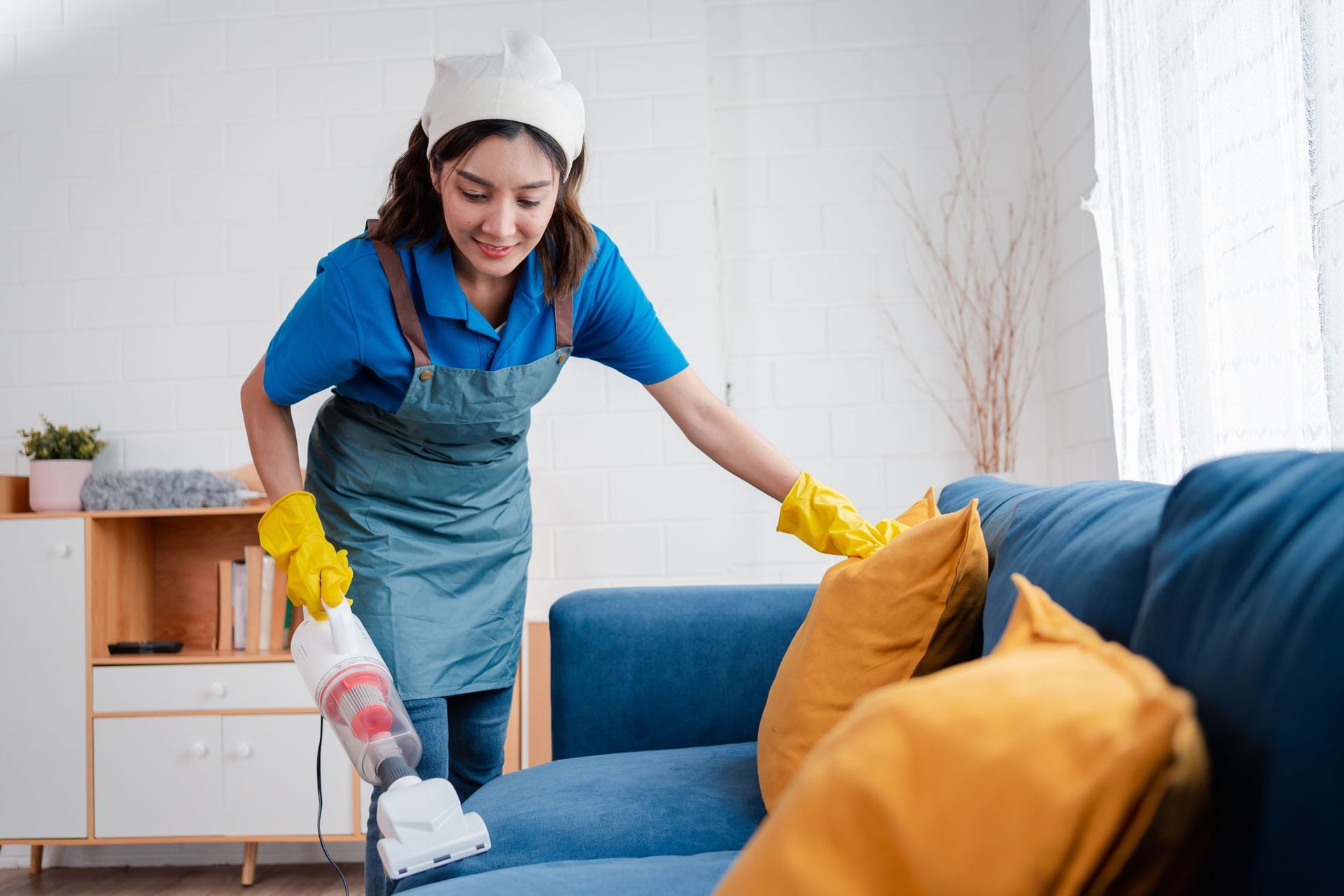 A woman is cleaning a couch with a vacuum cleaner in a living room.