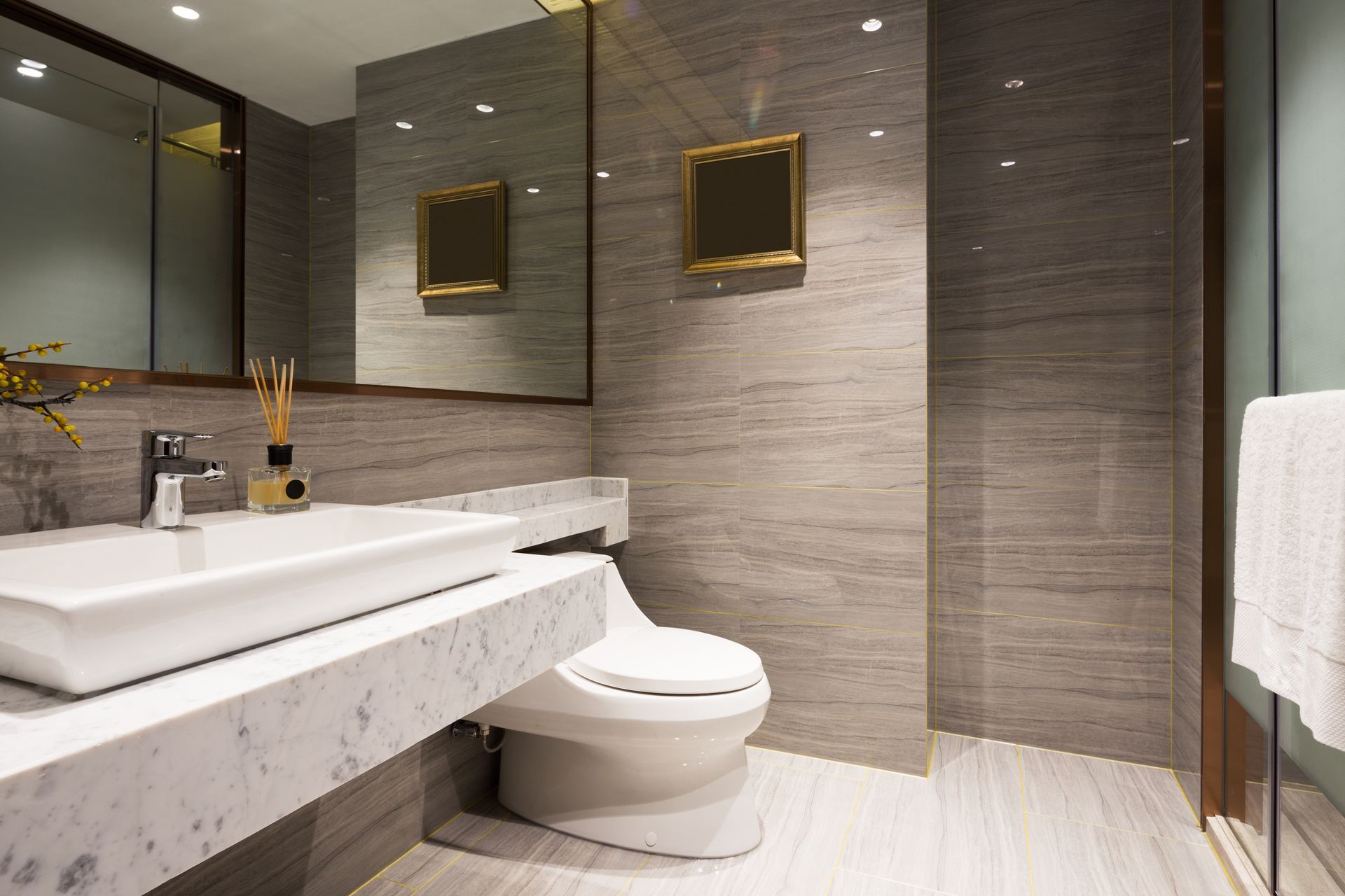 Modern bathroom with marble countertop, rectangular sink, and toilet; gray tiled walls.