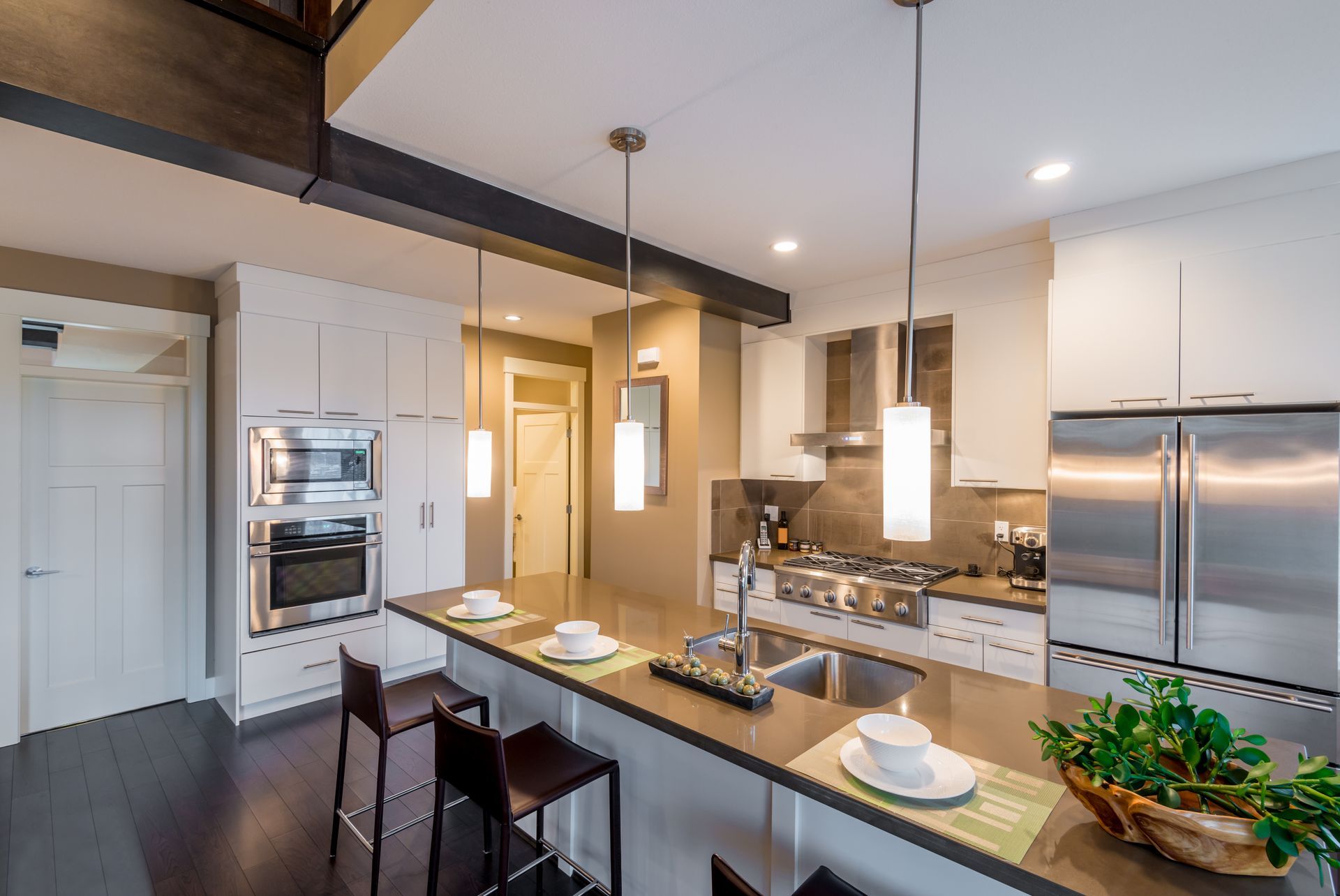 Modern kitchen with island, stainless steel appliances, white cabinets, dark wood floors, and pendant lighting.