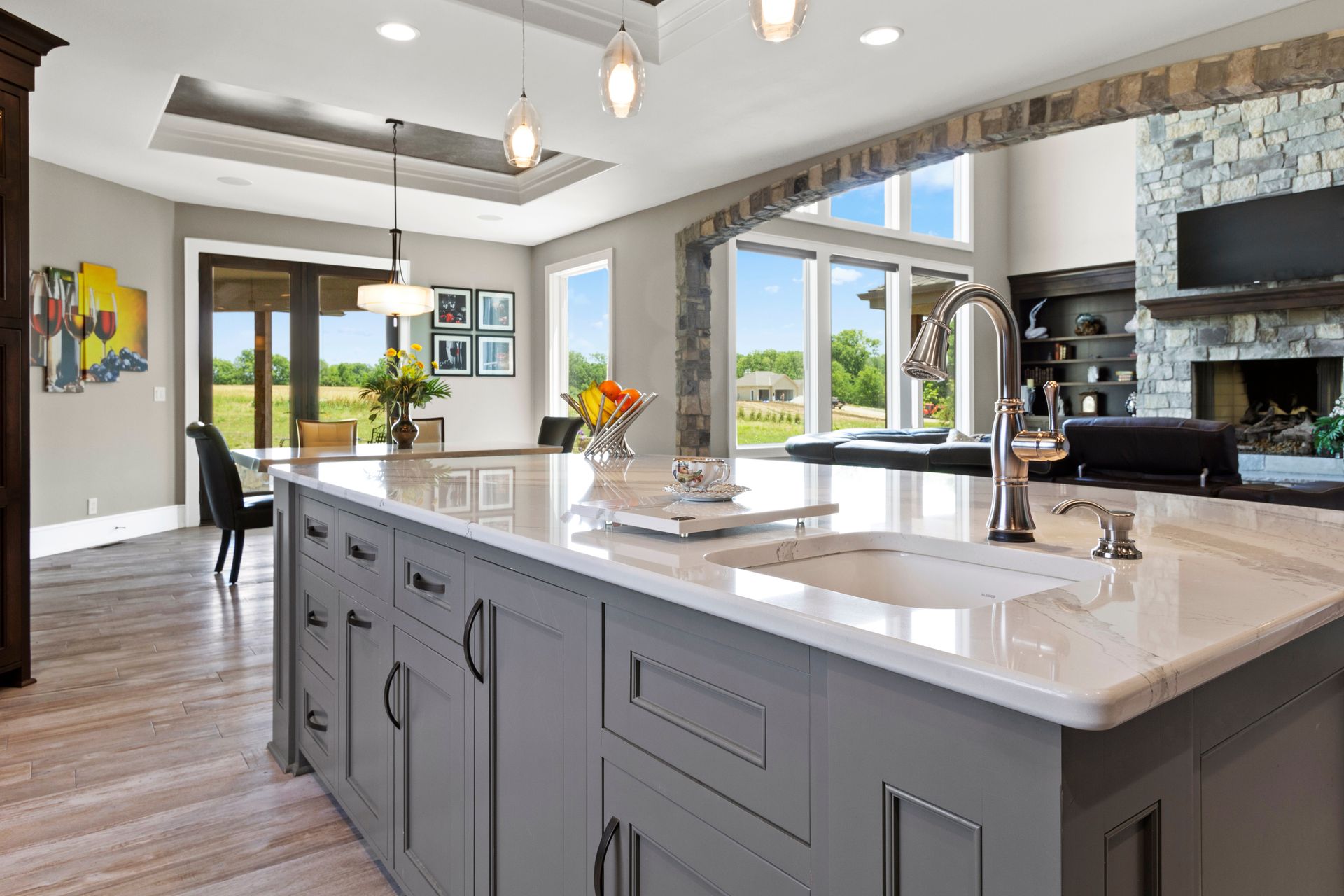 Gray kitchen island with white countertop in modern kitchen with archway to living room.