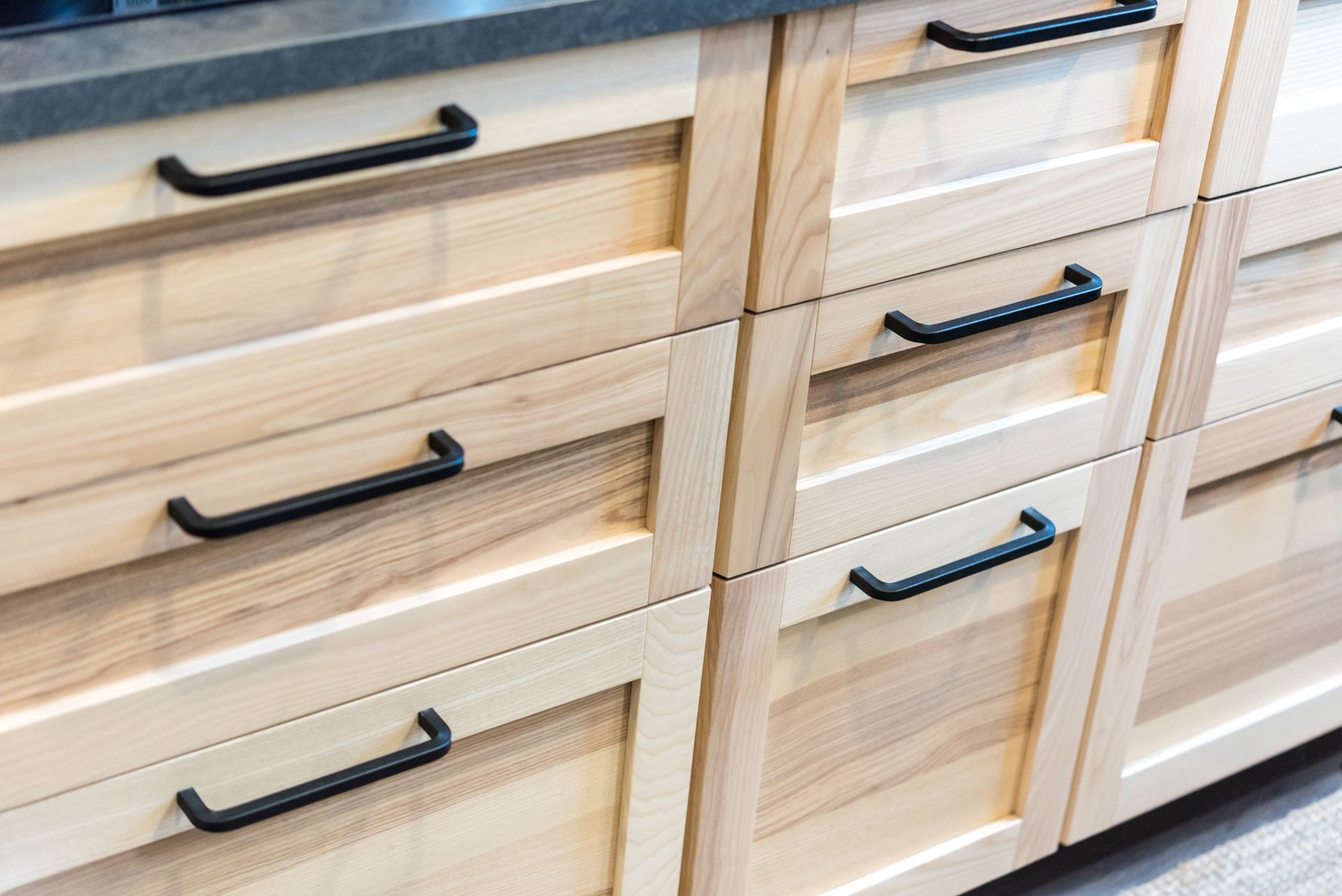 Light wood kitchen cabinets with black handles.