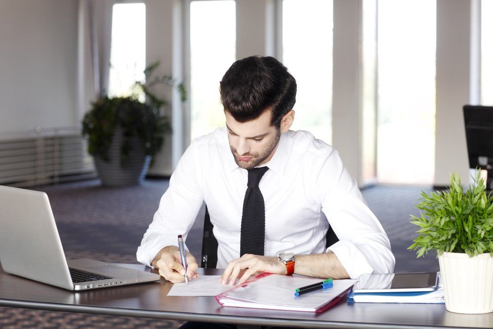 Man in White Shirt and Tie Writing at A Desk in An Office — Freedom Wealth Solutions In Mornington, VIC